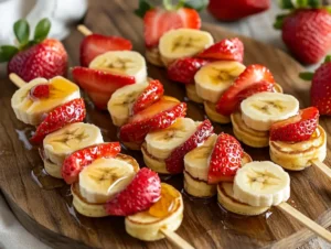 Mini pancakes threaded on skewers with strawberries and bananas.