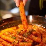 Bowl of spicy potato noodles garnished with herbs and chilies