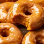 Delicious vegan pumpkin donuts on a wooden table showcasing their warm color and texture.